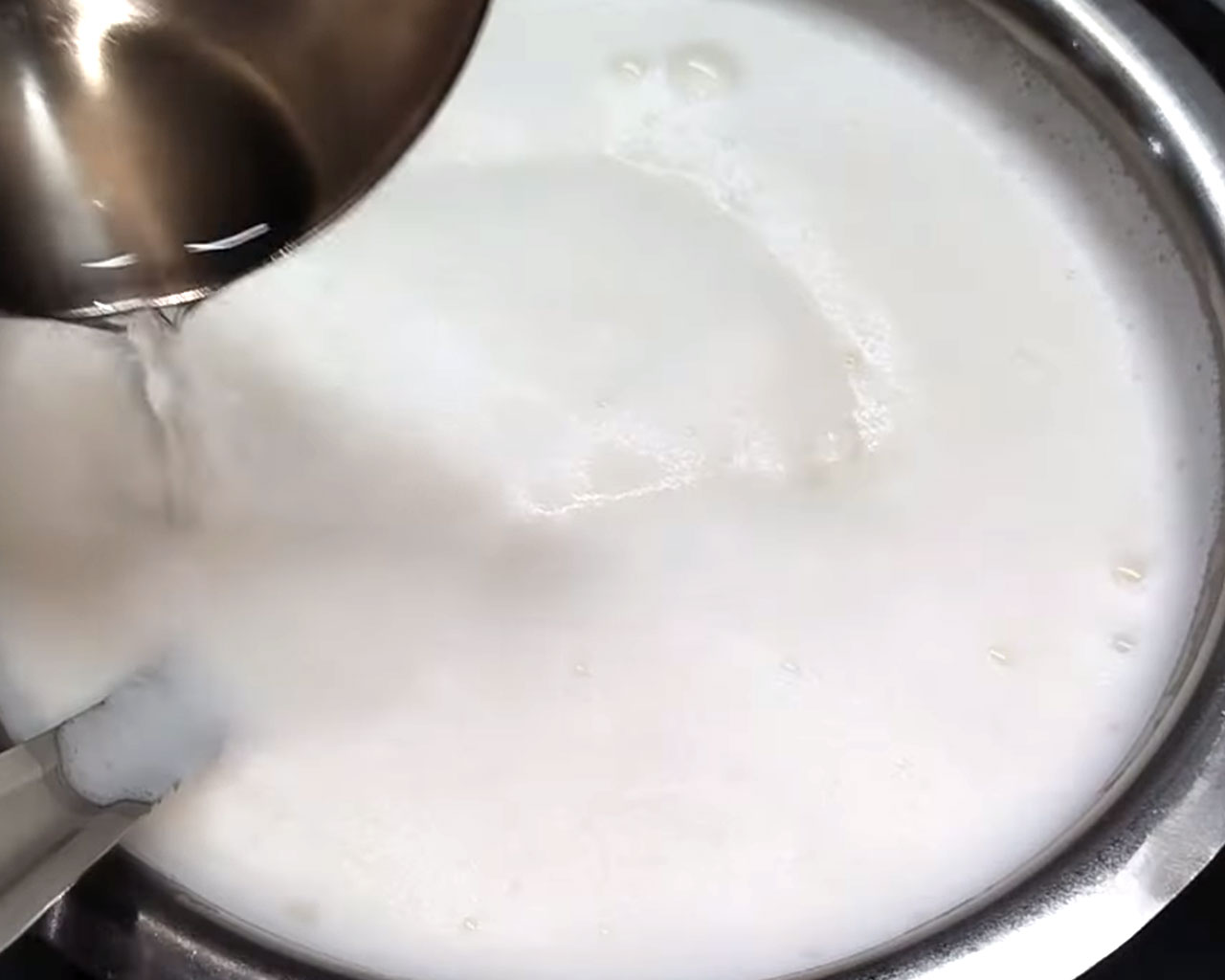 Adding vinegar slowly to boiling milk with a slotted spoon to curdle milk for paneer.