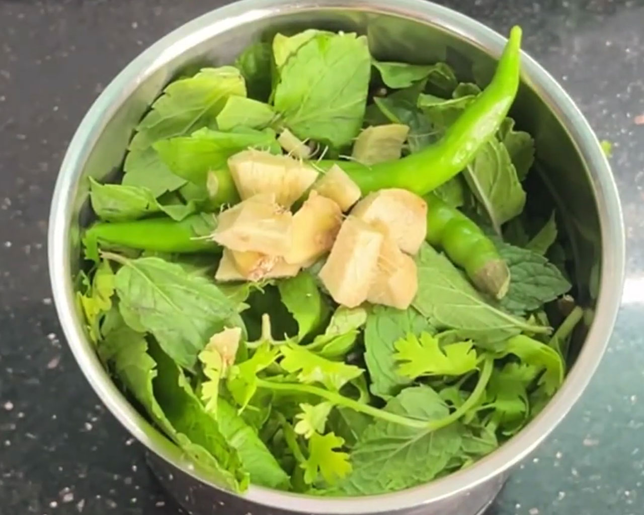 Green chilies and chopped ginger added to mint and coriander leaves in a grinder jar