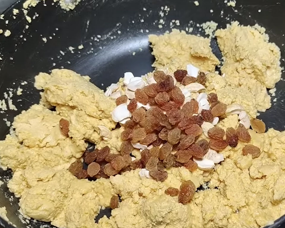 Adding chopped cashew nuts and raisins to roasted besan and ghee mixture for Indian sweet ladoo
