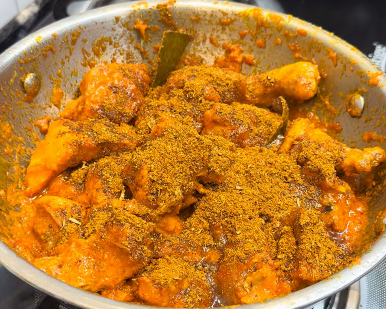 Ground Indian chicken masala being mixed into chicken curry in a pan