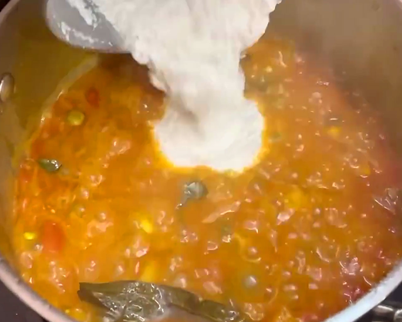 Coconut paste being stirred into cooked vegetables to create creamy coconut-based kurma.