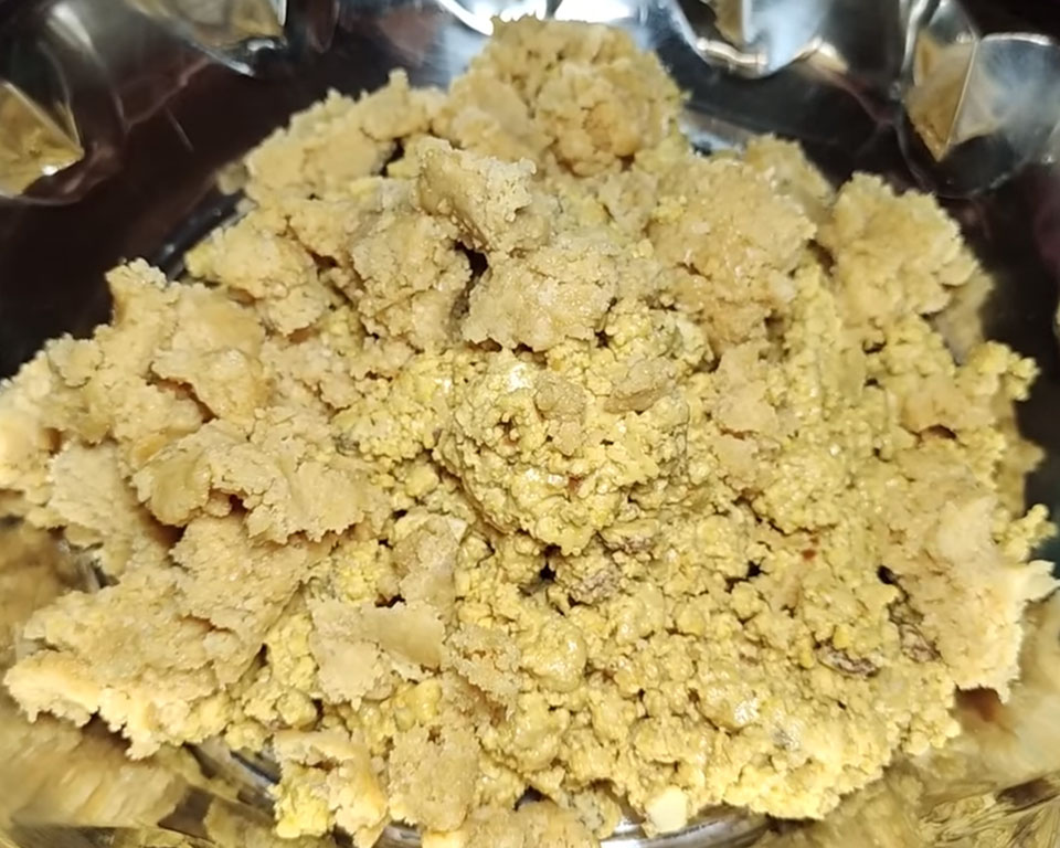 Kneading grated jaggery into warm roasted besan mixture by hand to sweeten Indian mithai ladoos