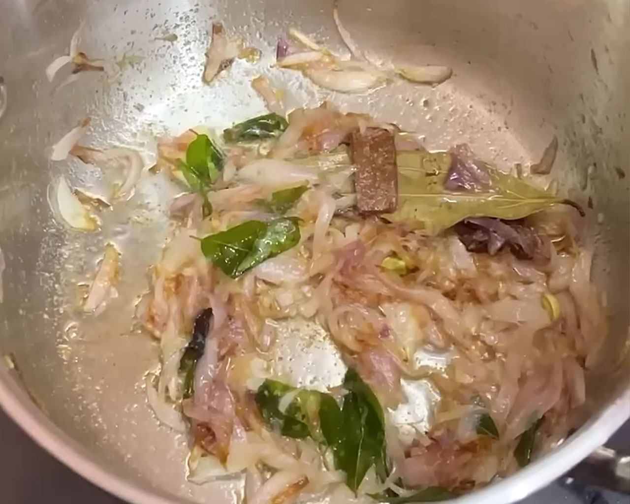 Finely chopped onions and curry leaves being sautéed for preparing vegetable kurma