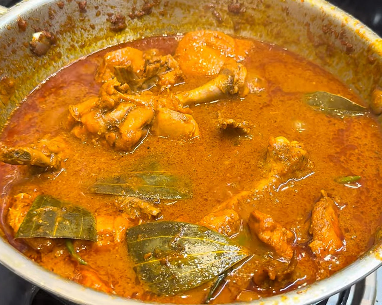 Chicken curry simmering in water on medium flame to thicken the gravy