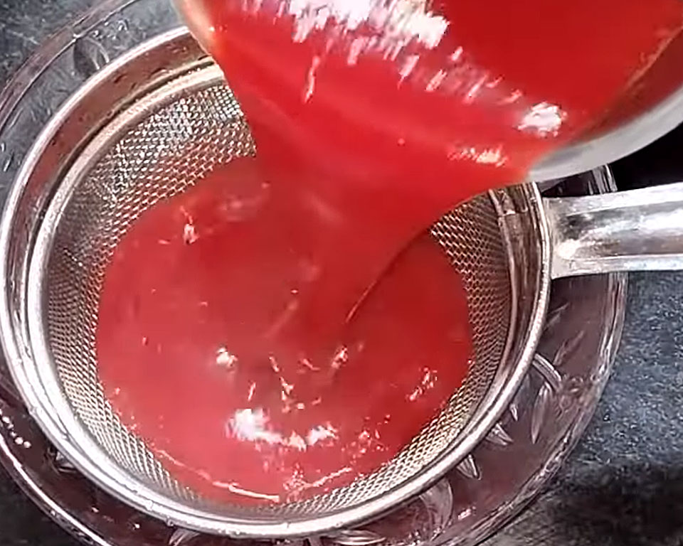 Straining boiled tomato mixture through a sieve to get smooth soup texture.