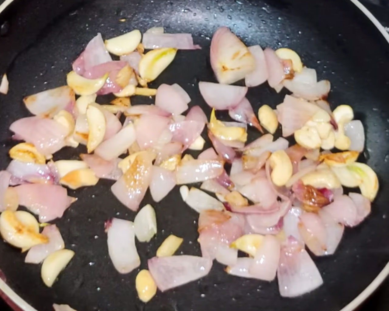 Chopped onions, garlic cloves, and cashew nuts sautéing in oil for making matar paneer masala paste
