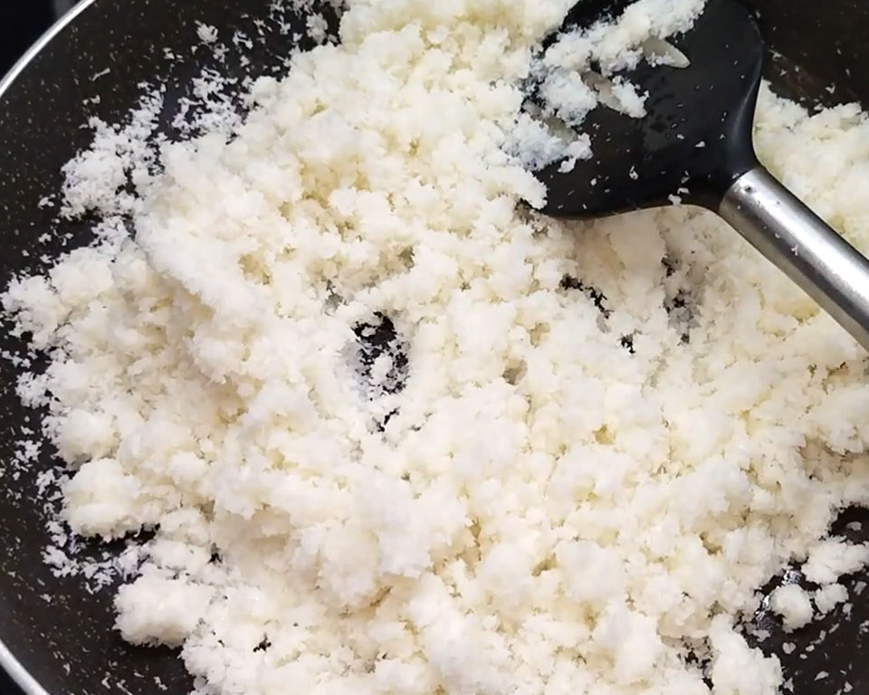 Adding full-fat milk and cream to roasted coconut for ladoo mixture