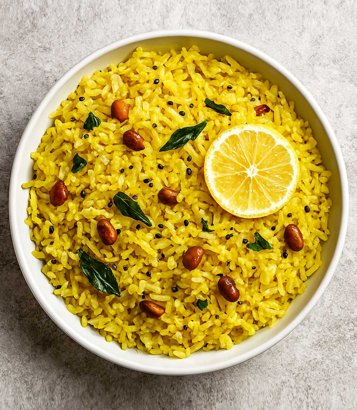 Indian lemon rice dish with peanuts, curry leaves, and lemon wedge on the side, a flavorful and tangy vegetarian meal option from South India.