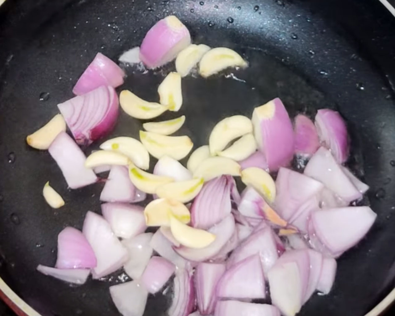 Chopped onions, garlic cloves sautéing in oil for making matar paneer masala paste