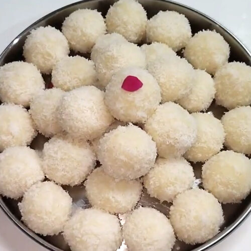 Shaping warm coconut mixture into round ladoos rolled in extra desiccated coconut