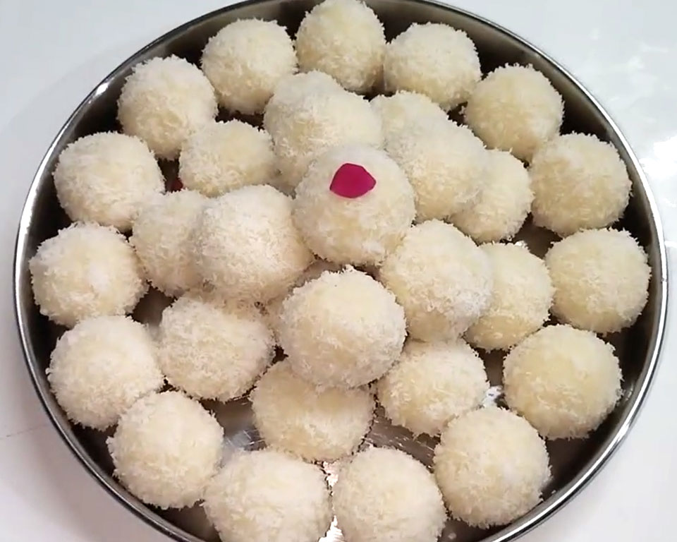 Shaping warm coconut mixture into round ladoos rolled in extra desiccated coconut