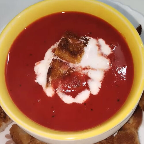 Serving Indian tomato soup in a bowl garnished with coriander leaves and crispy croutons.