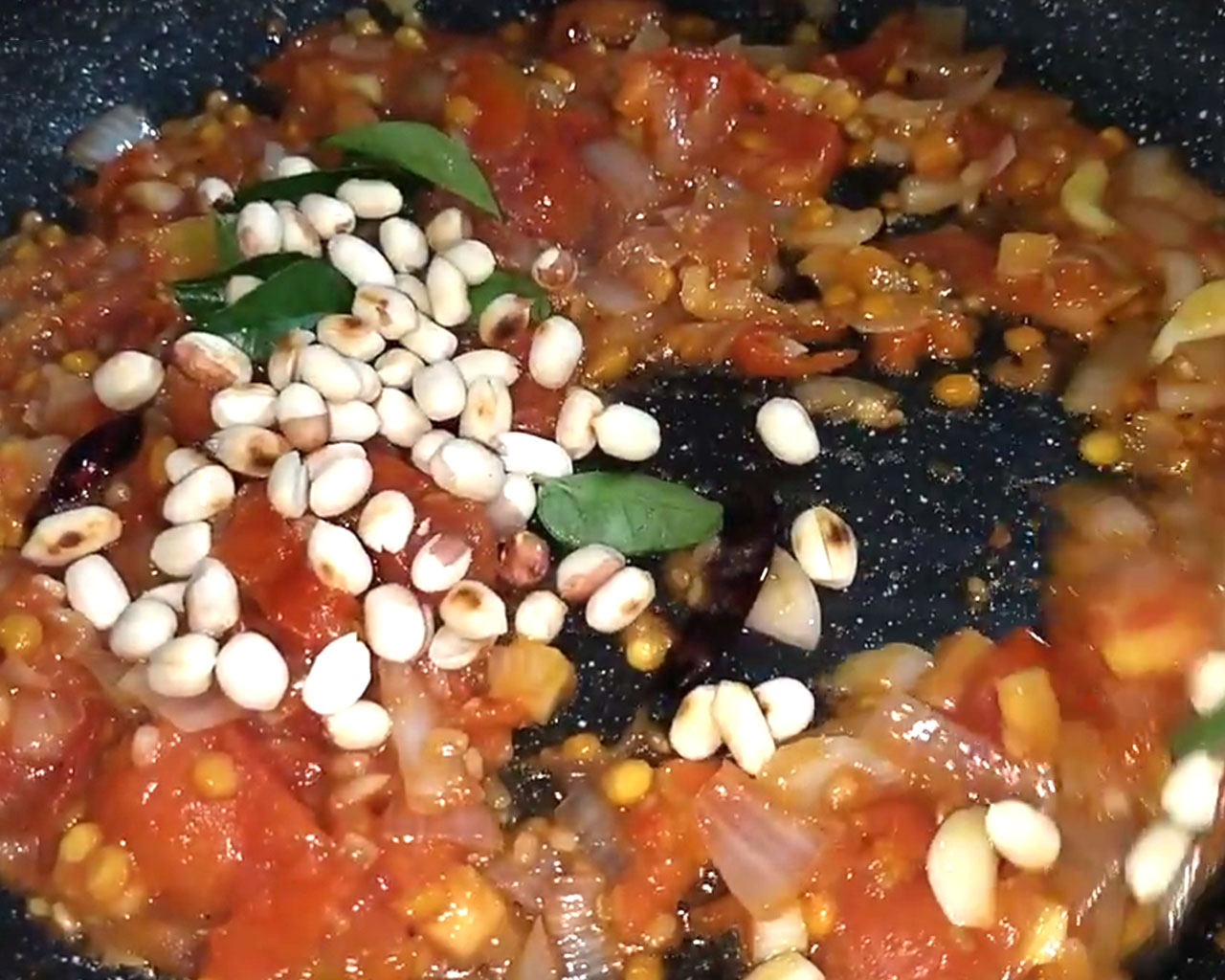 Adding fresh curry leaves and roasted peanuts to tomato mixture in pan