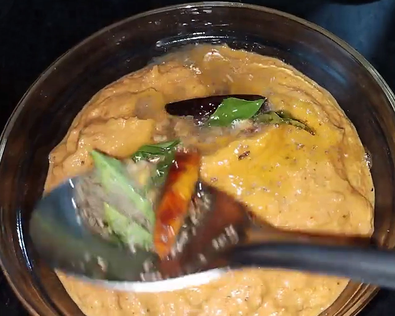 Pouring hot tempering over freshly ground tomato chutney in serving bowl