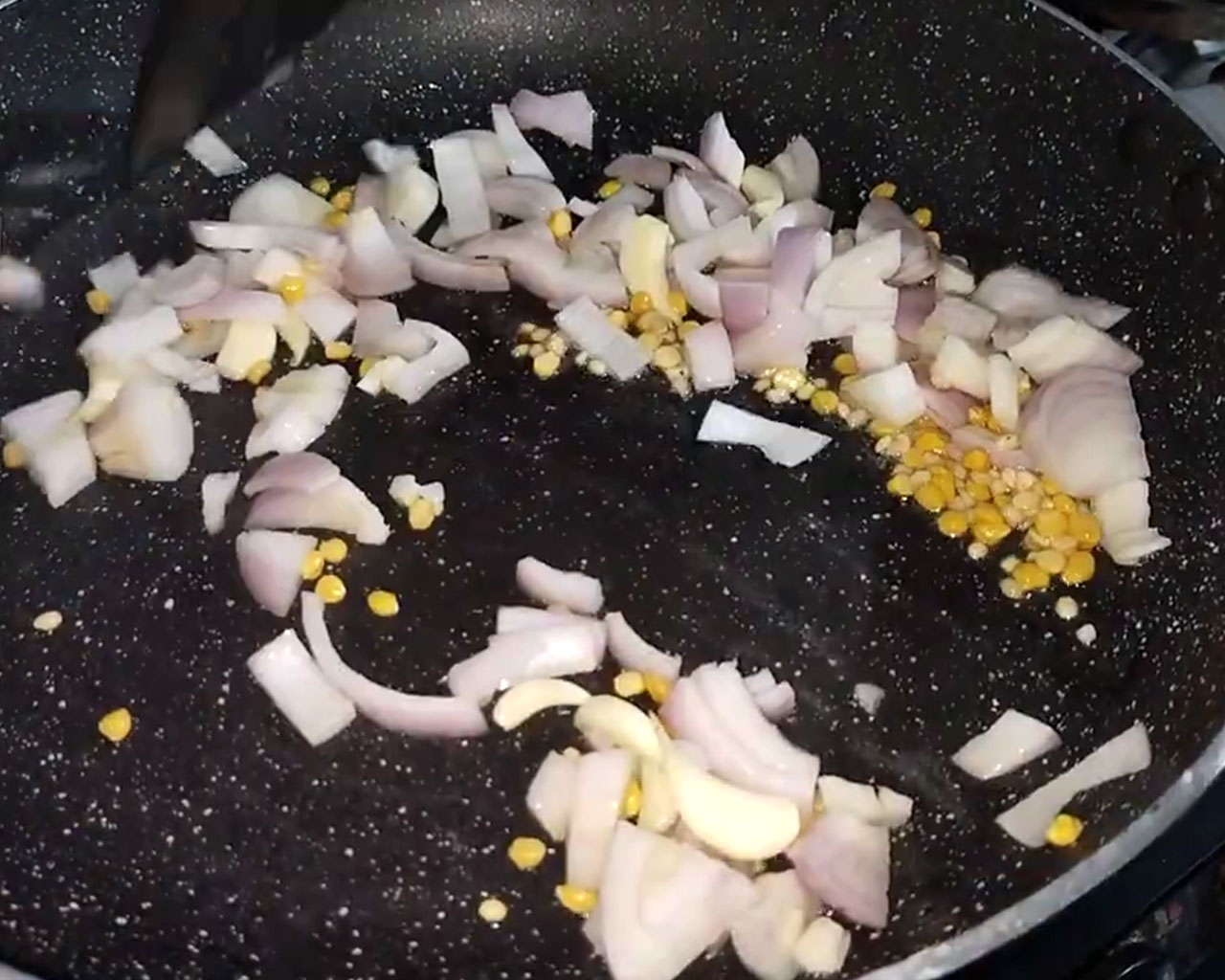 Sautéing urad dal, chana dal, garlic cloves, and chopped onions in hot oil