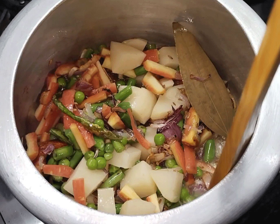 Chopped carrots, green beans, and potatoes added to sautéed onions in cooker