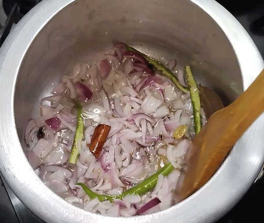 Frying onions and spices for masala pulao in cooker.