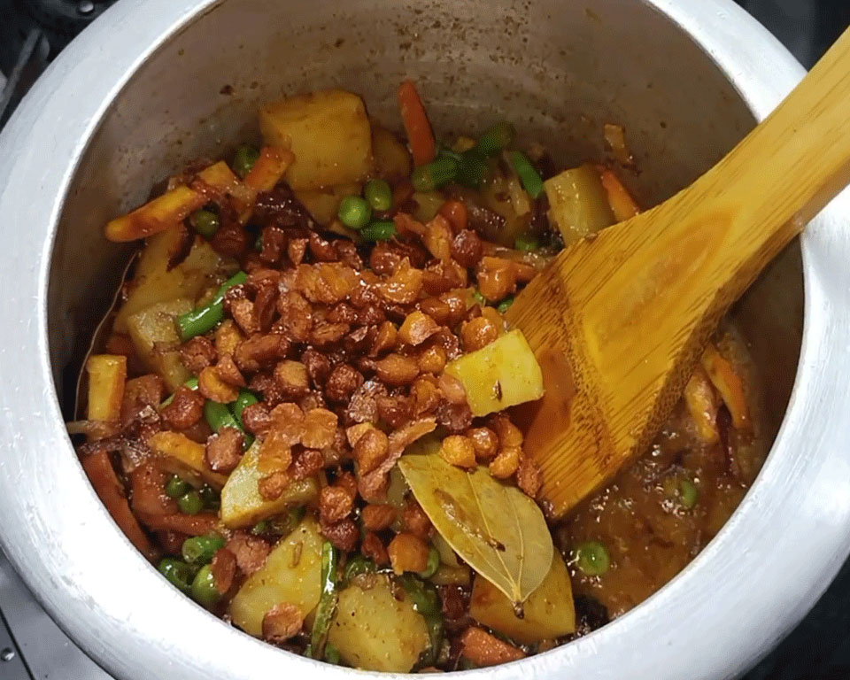 Fried moong dal badi being mixed with vegetables and spices in the cooker