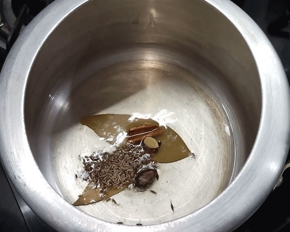 Whole spices like bay leaf, cinnamon, and cumin seeds sizzling in oil in a pressure cooker