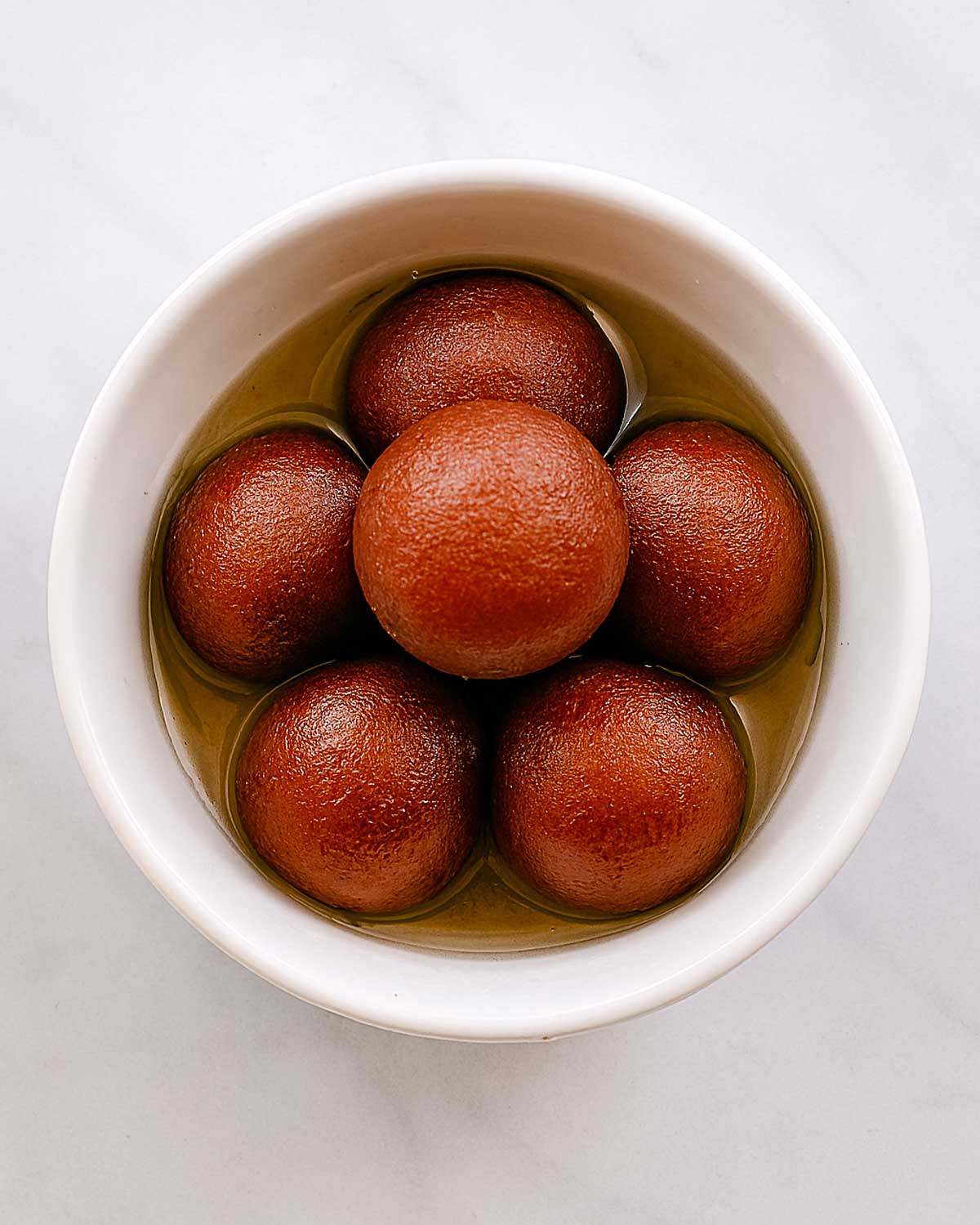 Soft and spongy gulab jamun served in a bowl of sugar syrup, sweet Indian dessert.