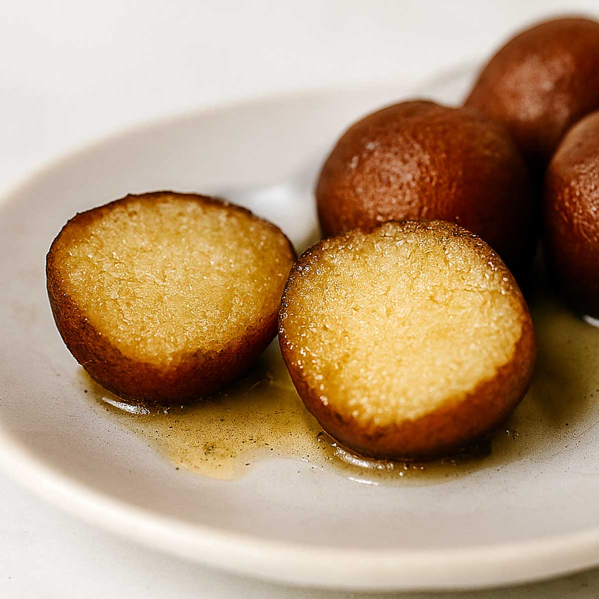 Close-up of juicy Indian gulab jamun mithai served warm in a white plate, inside view half gulab jamun.