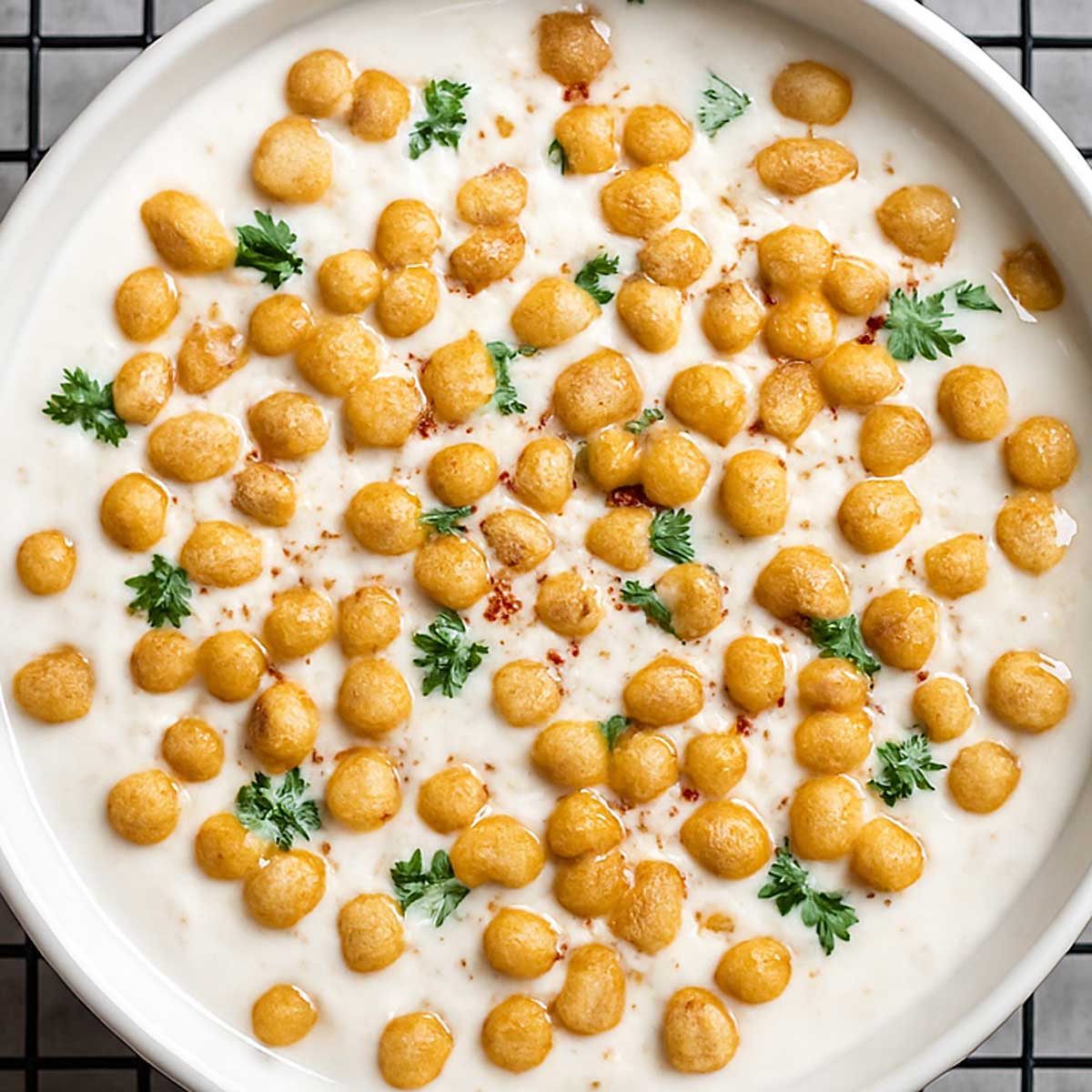 Close-up of boondi raita showing creamy yogurt, crispy boondi, and fresh herbs, served as a refreshing side dish for Indian curries and biryani.