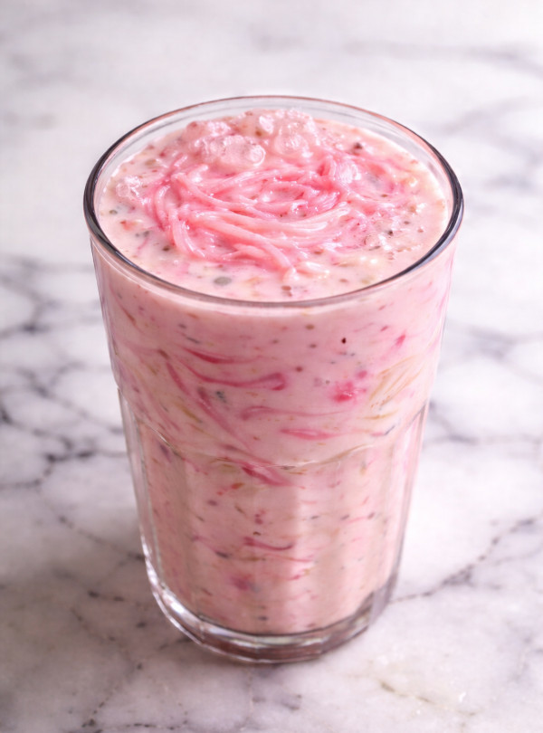 Layered rose falooda dessert in tall glass with sabja seeds, vermicelli noodles, sweet milk and syrup mixed, ready for vanilla ice cream topping